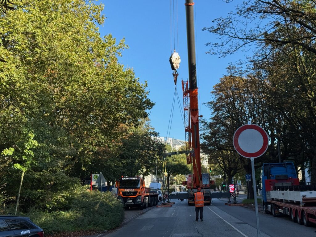 Eine Strasse muss gesperrt werden, weil das große Klimagerät mit einem Kran aufs Dach transportiert wird.